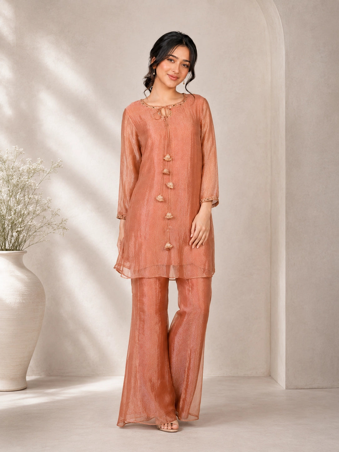 Woman wearing a peach embroidered kurta with gold tassels and a tie-neck detail.