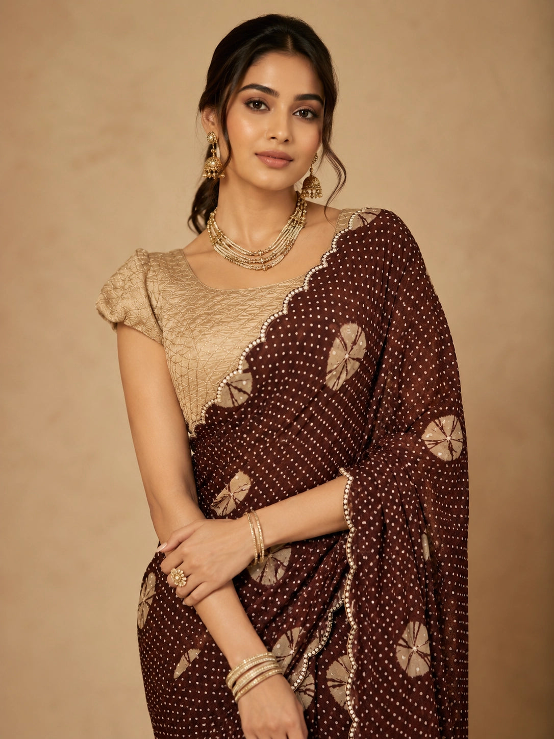 Woman in maroon bandhani saree with golden blouse and traditional jewelry.