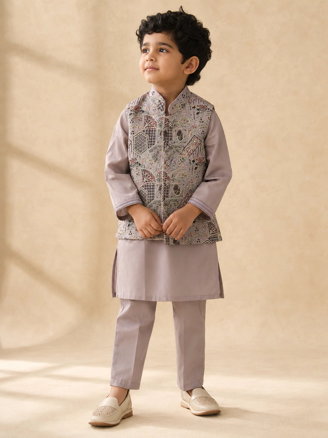 Young boy wearing a levendar kurta pajama with an intricately patterned waistcoat.