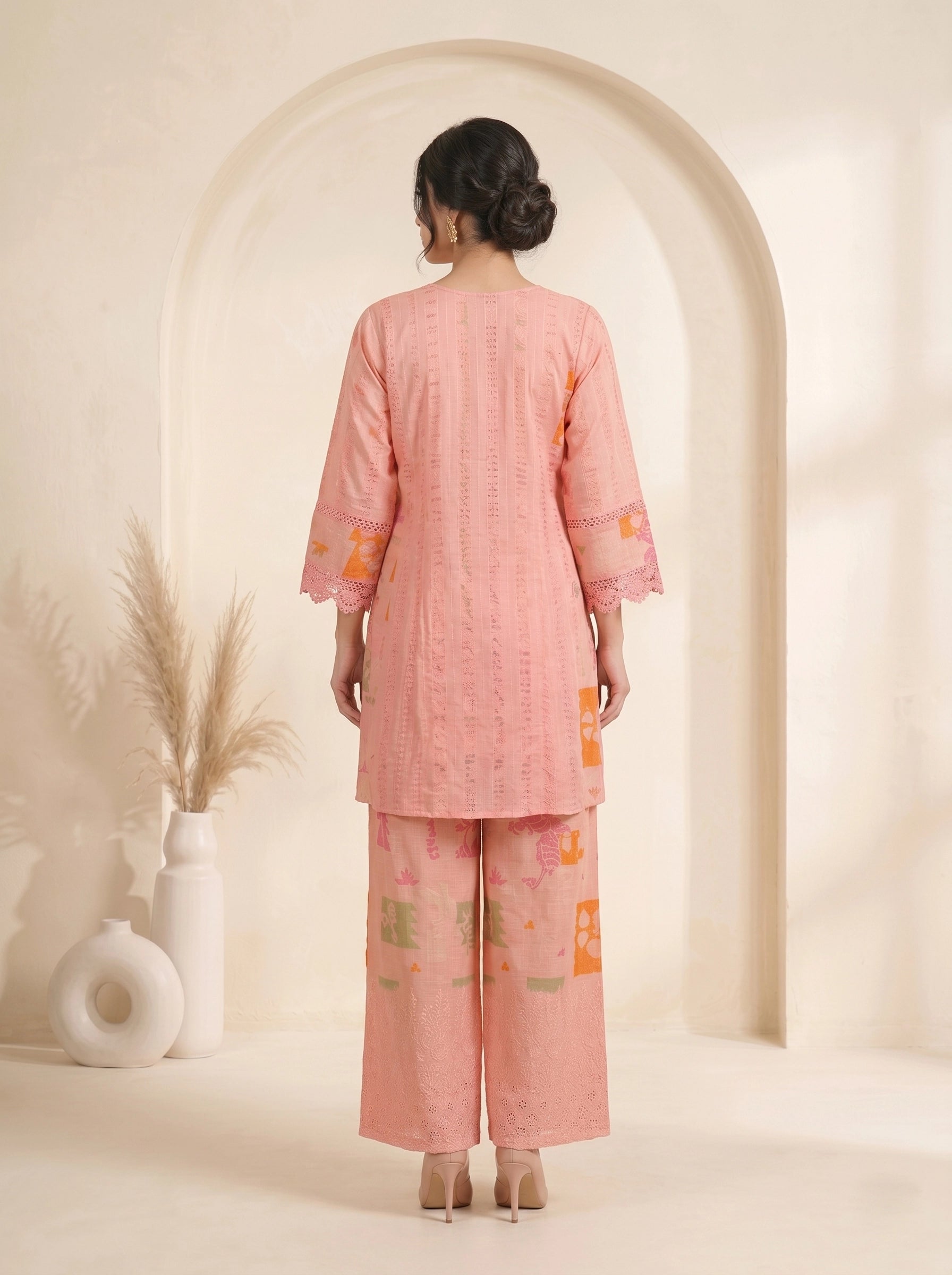 Woman wearing a pink printed cotton kurti set with palazzo pants and a dupatta, featuring eyelet details and block prints.