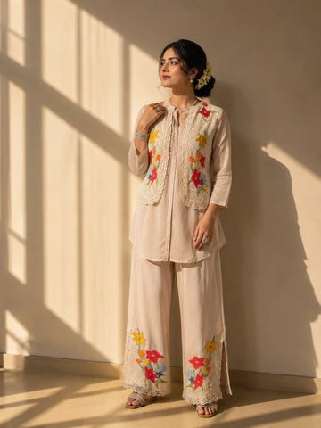 Woman in a beige kurta set with a short floral embroidered jacket and palazzo pants.
