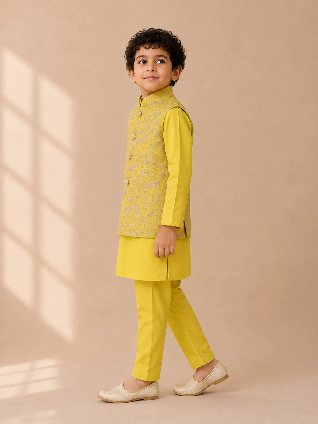 Young boy wearing a bright yellow kurta pajama set with an embroidered waistcoat.