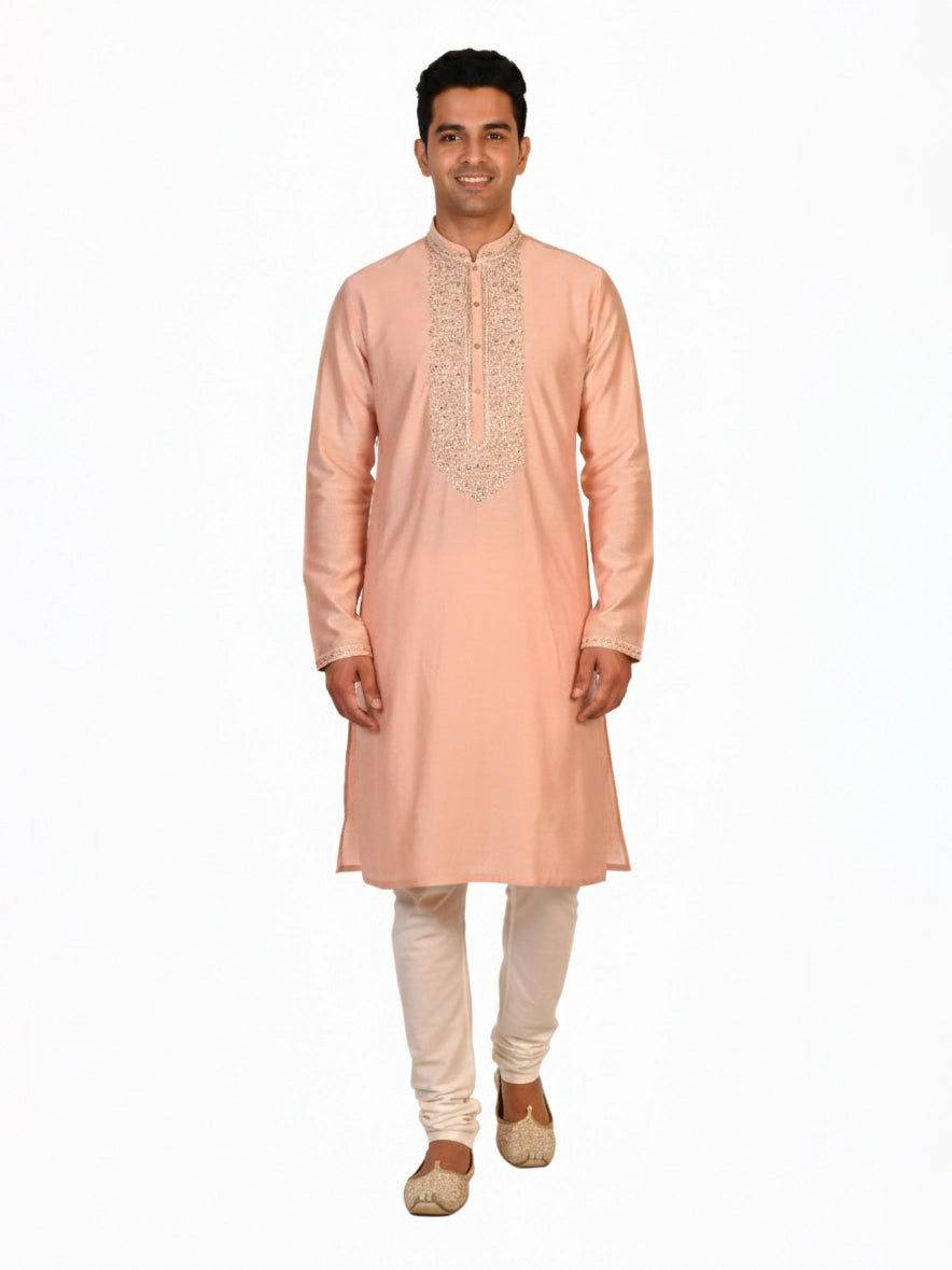 Man wearing a peach silk Kurta Pajama with intricate embroidery on the neckline and cream churidar pants.