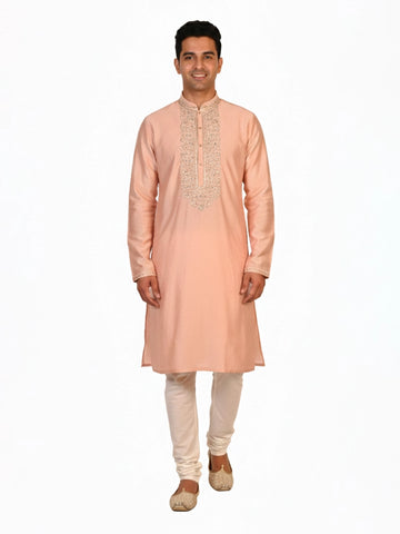 Man wearing a peach silk Kurta Pajama with intricate embroidery on the neckline and cream churidar pants.