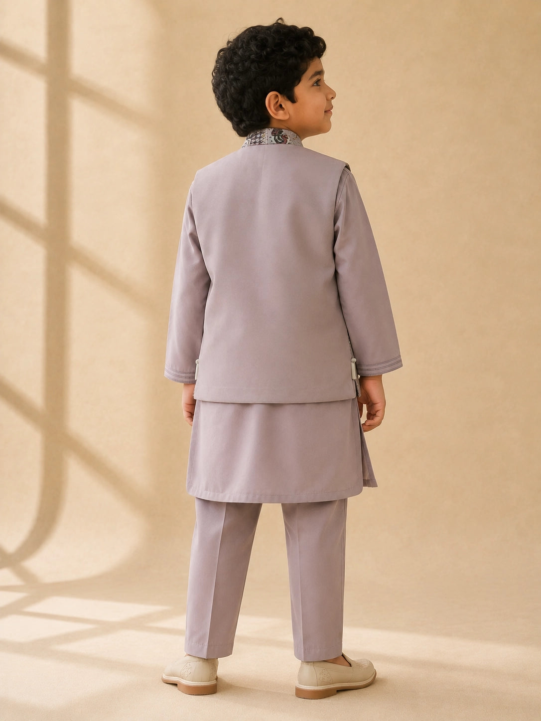Young boy wearing a levendar kurta pajama with an intricately patterned waistcoat.