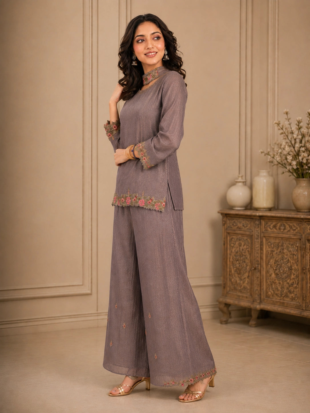 Woman wearing a pink embroidered choker neck Sharara with floral details on sleeves and hem.