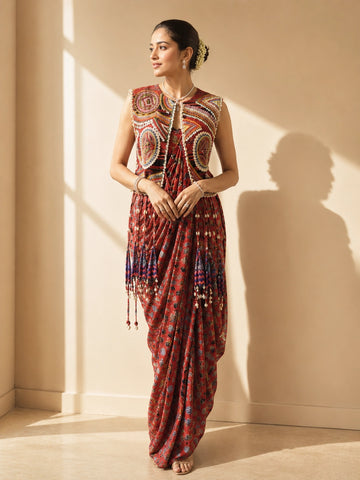 Woman wearing a red printed draped saree and an intricately embroidered sleeveless jacket.