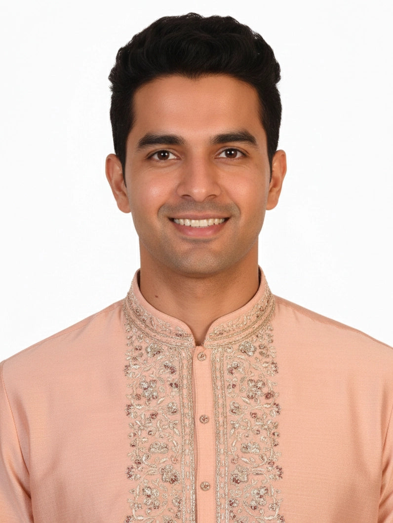 Man wearing a peach silk Kurta Pajama with intricate embroidery on the neckline and cream churidar pants.