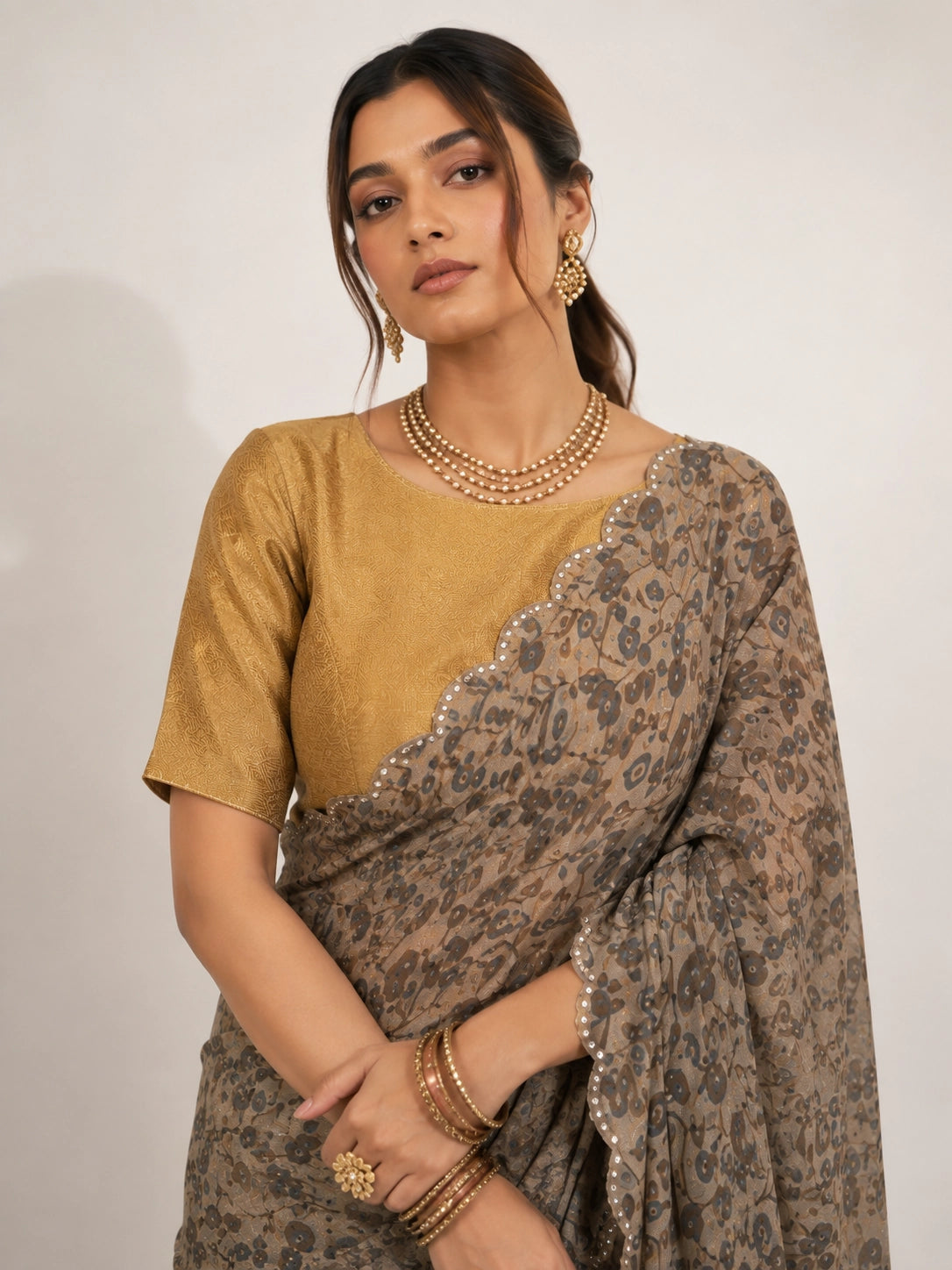 Woman wearing an elegant cream  printed saree with a gold blouse and embellished black pallu.