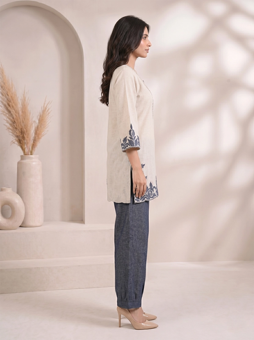 Woman wearing a beige embroidered V-neck kurta with dark blue palazzo pants, styled for a casual occasion.