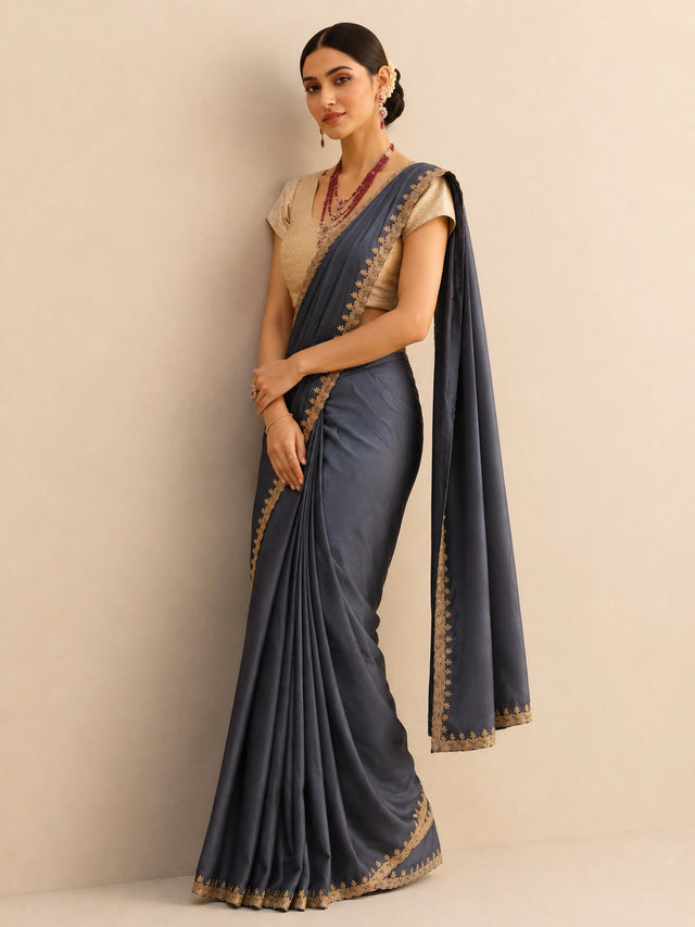 Woman wearing a flowing grey saree with an intricate golden border and a textured golden blouse.