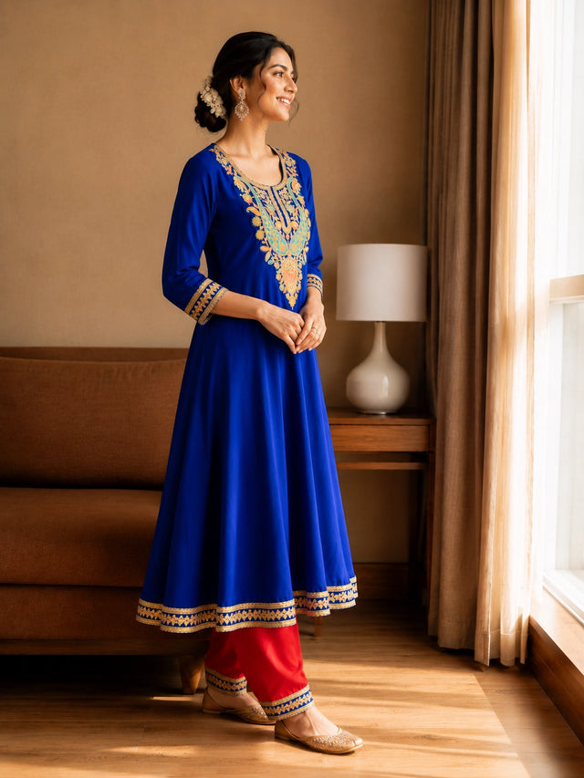 Woman in royal blue embroidered kurta with red pants, sitting by window.