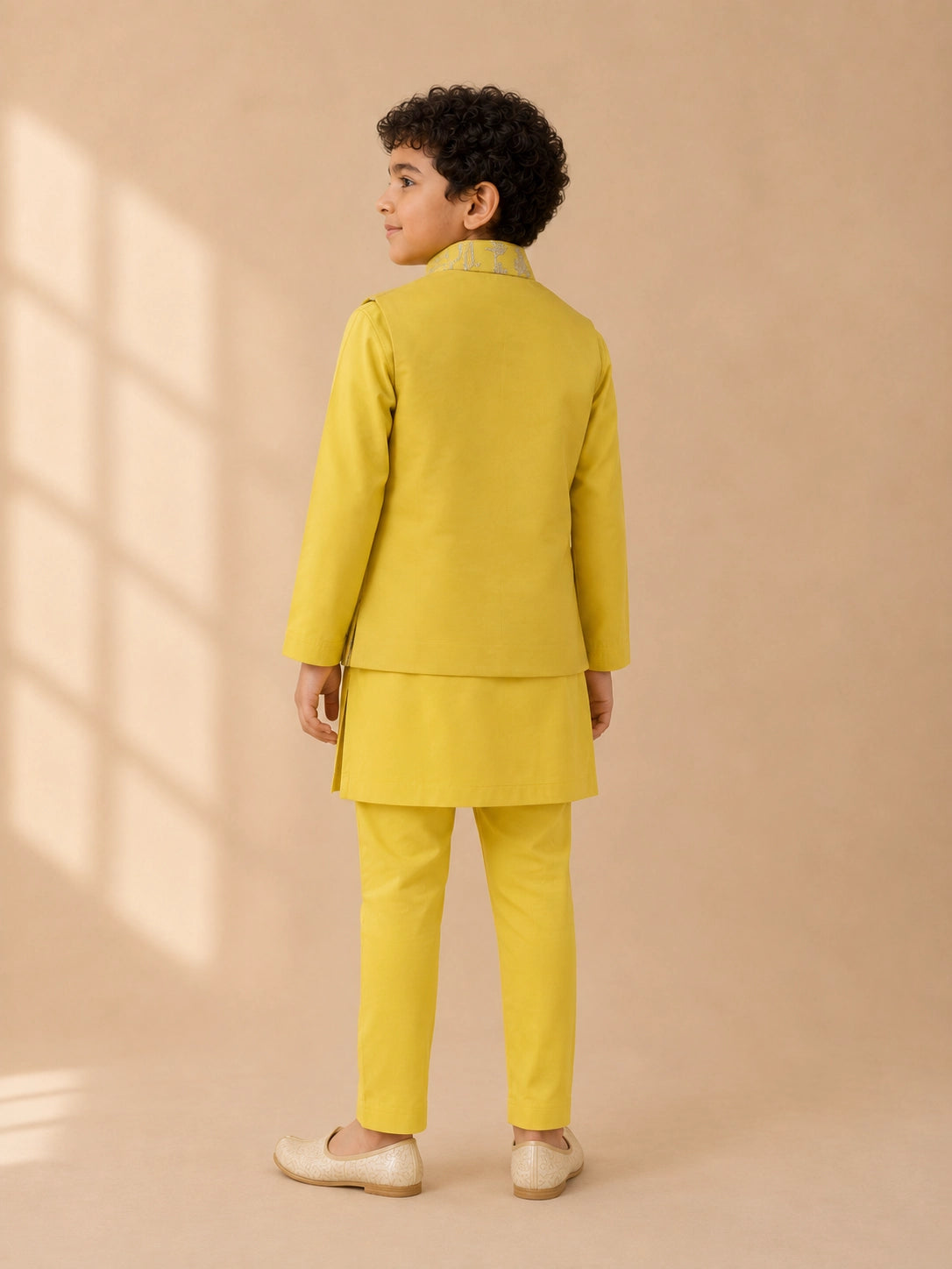 Young boy wearing a bright yellow kurta pajama set with an embroidered waistcoat.