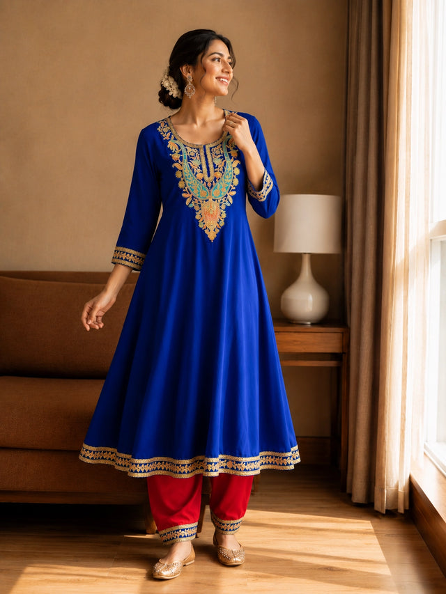 Woman in royal blue embroidered kurta with red pants, sitting by window.