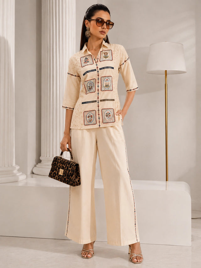 Woman wearing a cream embroidered shirt and wide-leg pants, sitting with a leopard print handbag.