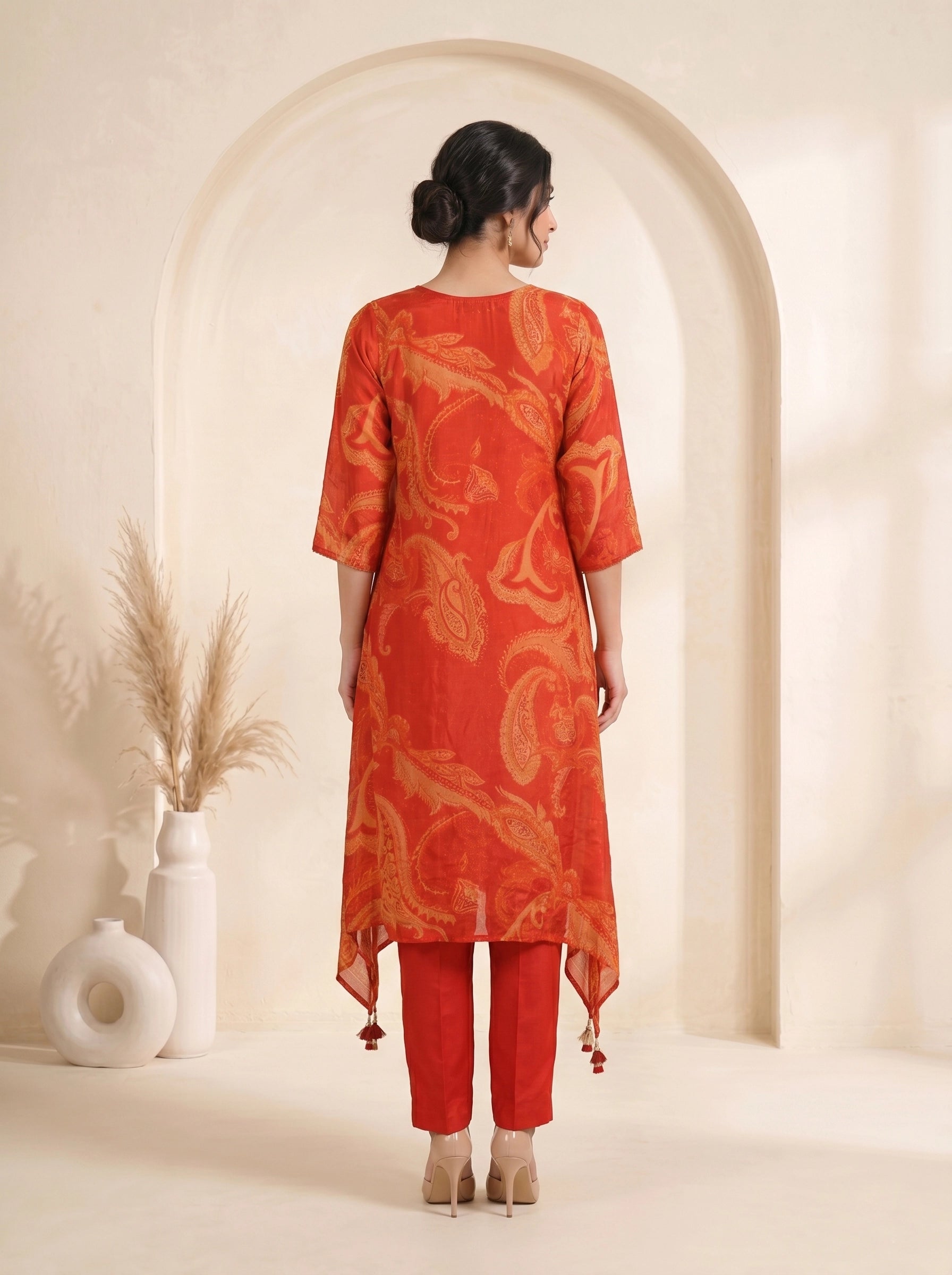 Woman wearing a vibrant orange kurti with paisley print and matching pants, adorned with neckline embellishments.