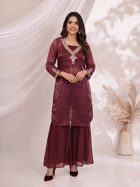 Woman wearing a maroon embroidered kurta with flowing sharara pants, featuring gold neckline and cuff details.