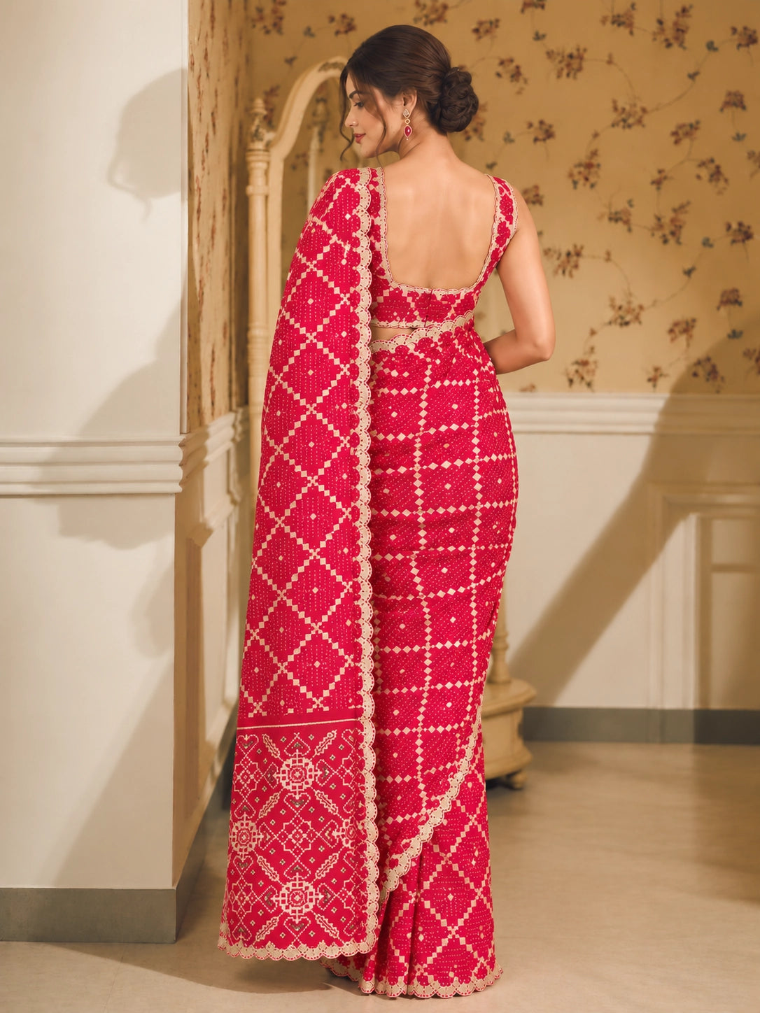 Woman in a vibrant red Bandhani saree with white patterns and scalloped border.