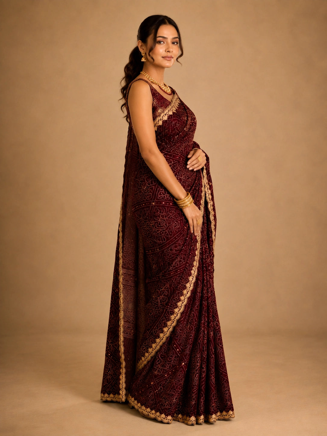 Woman in a maroon bandhani saree with intricate gold embroidery and border.