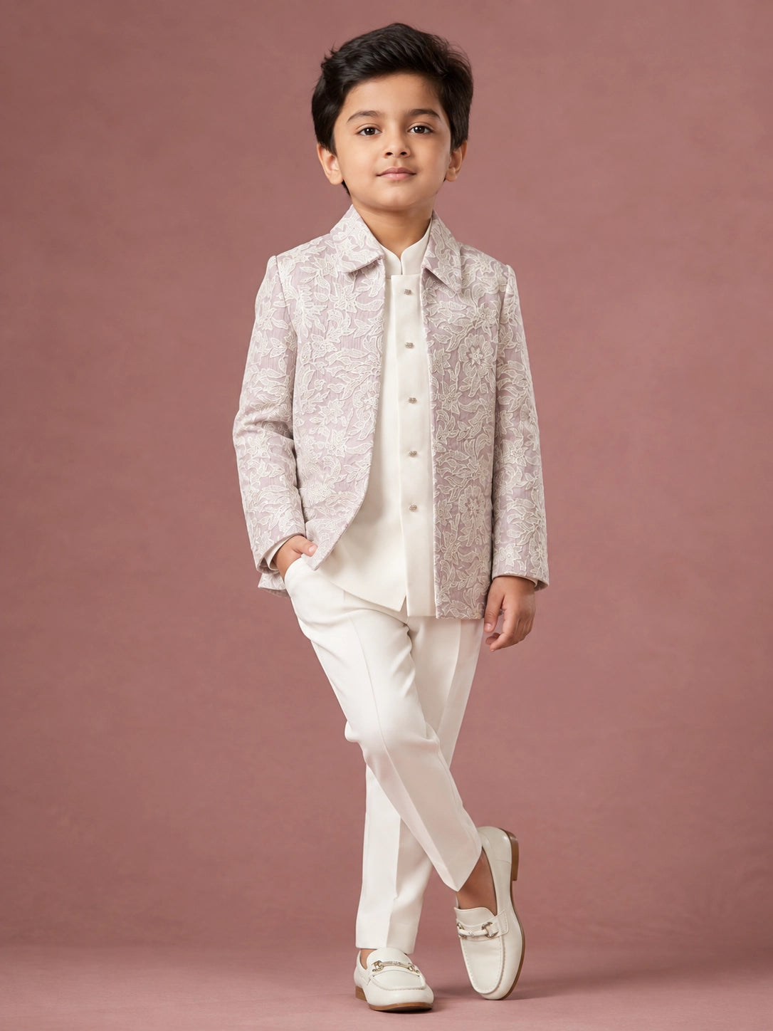 Young boy in a light pink patterned IndoWestern jacket, white kurta, and white trousers.