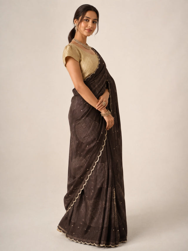 Woman in elegant brown saree with geometric patterns, scalloped border, and golden blouse.