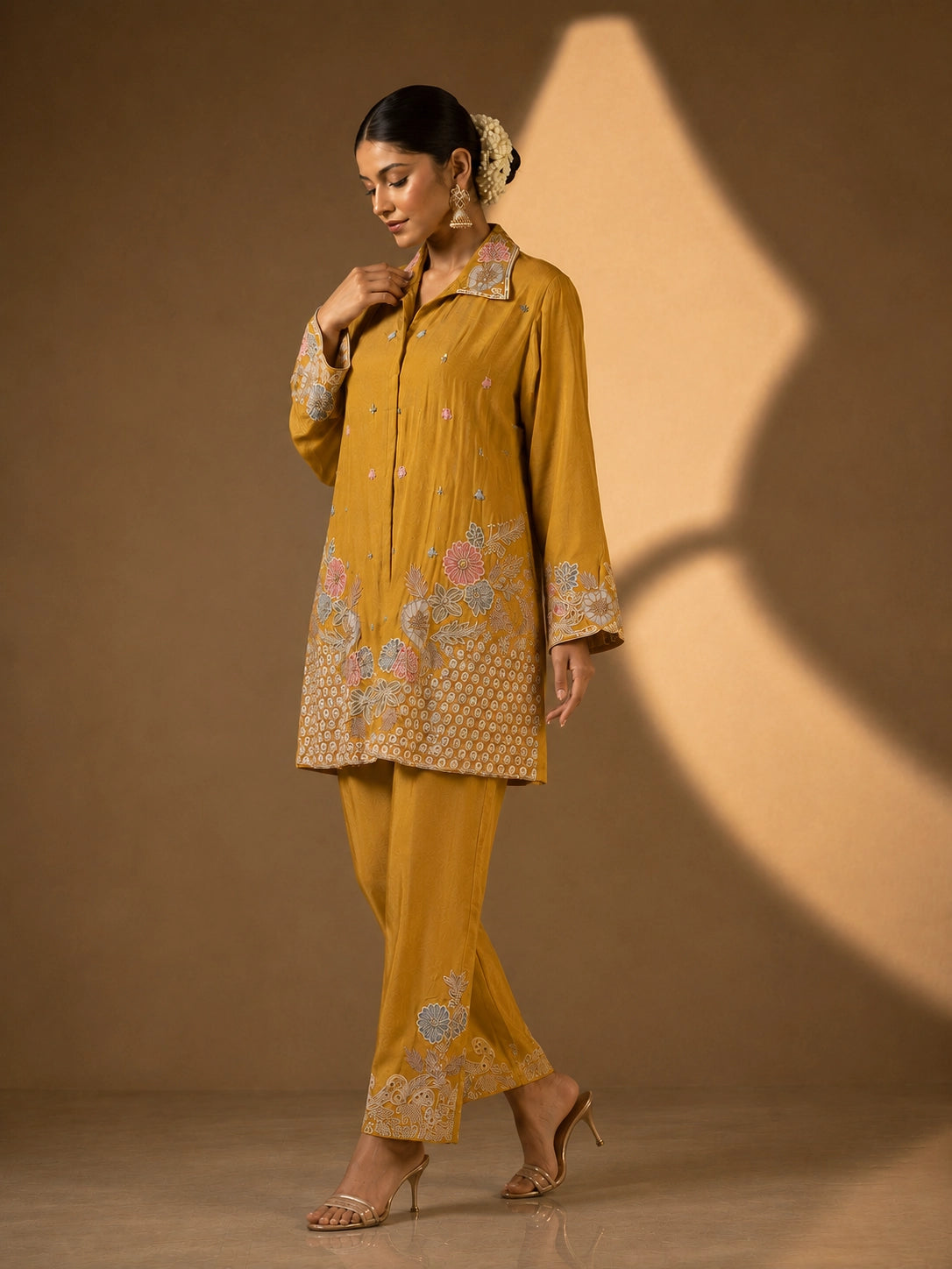 Model in a mustard embroidered kurti set with pastel floral patterns and matching pants.