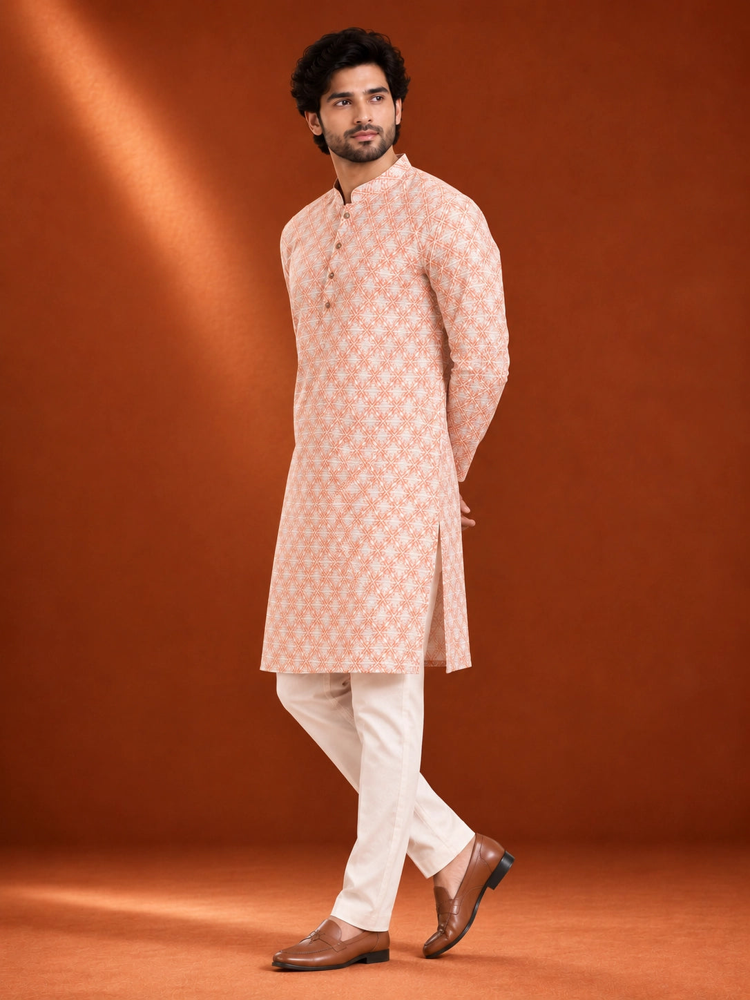 Man wearing an orange and white geometric printed kurta with white pajama and brown loafers.