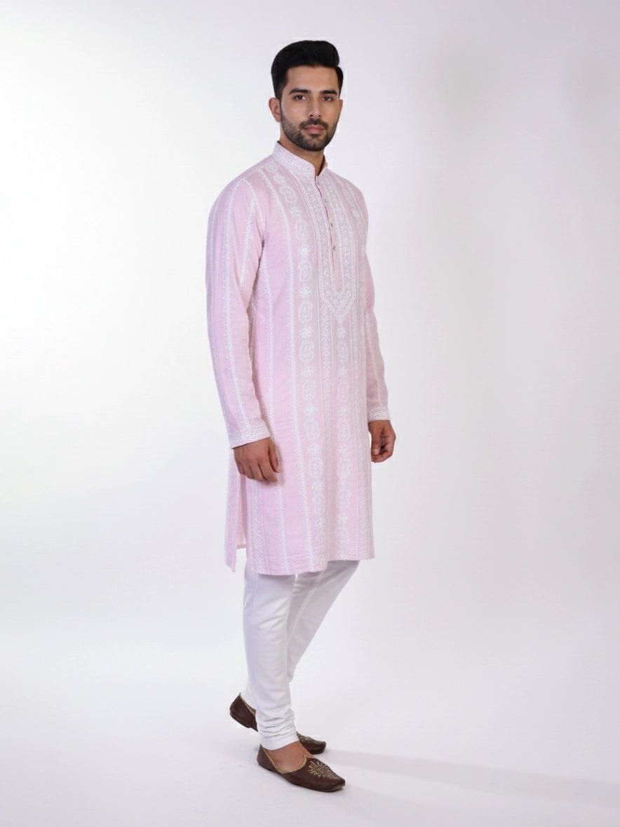 Man wearing a pink chikankari kurta with white churidar pants and brown embellished juttis.