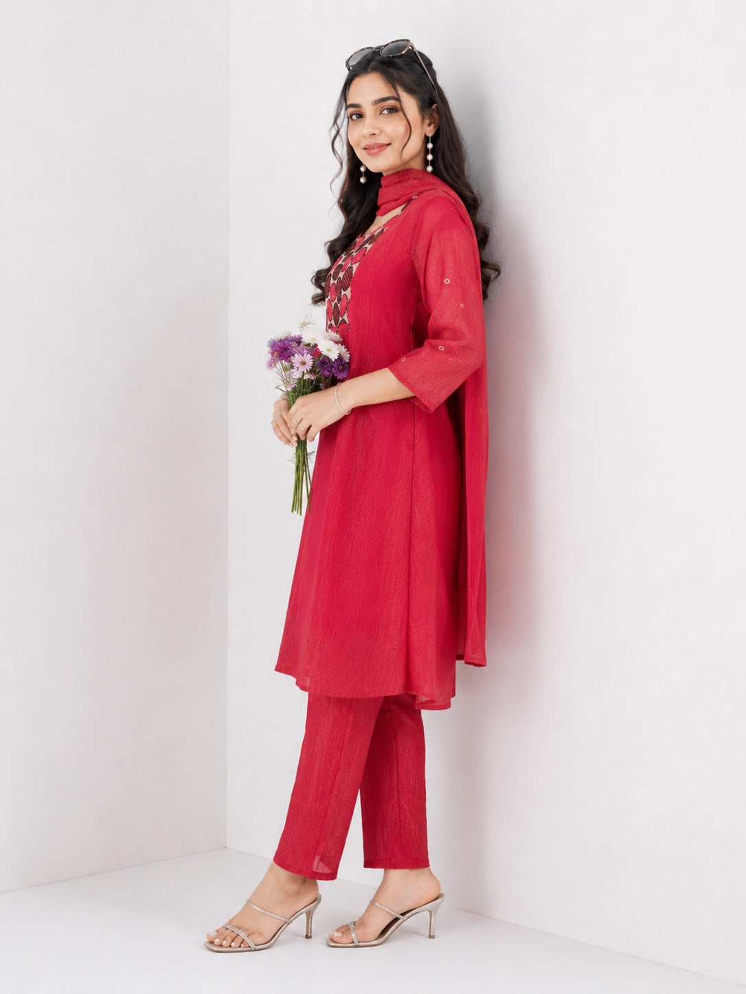 Woman wearing a Rani red Sharara with a geometric print yoke and matching dupatta, styled with pearl earrings.