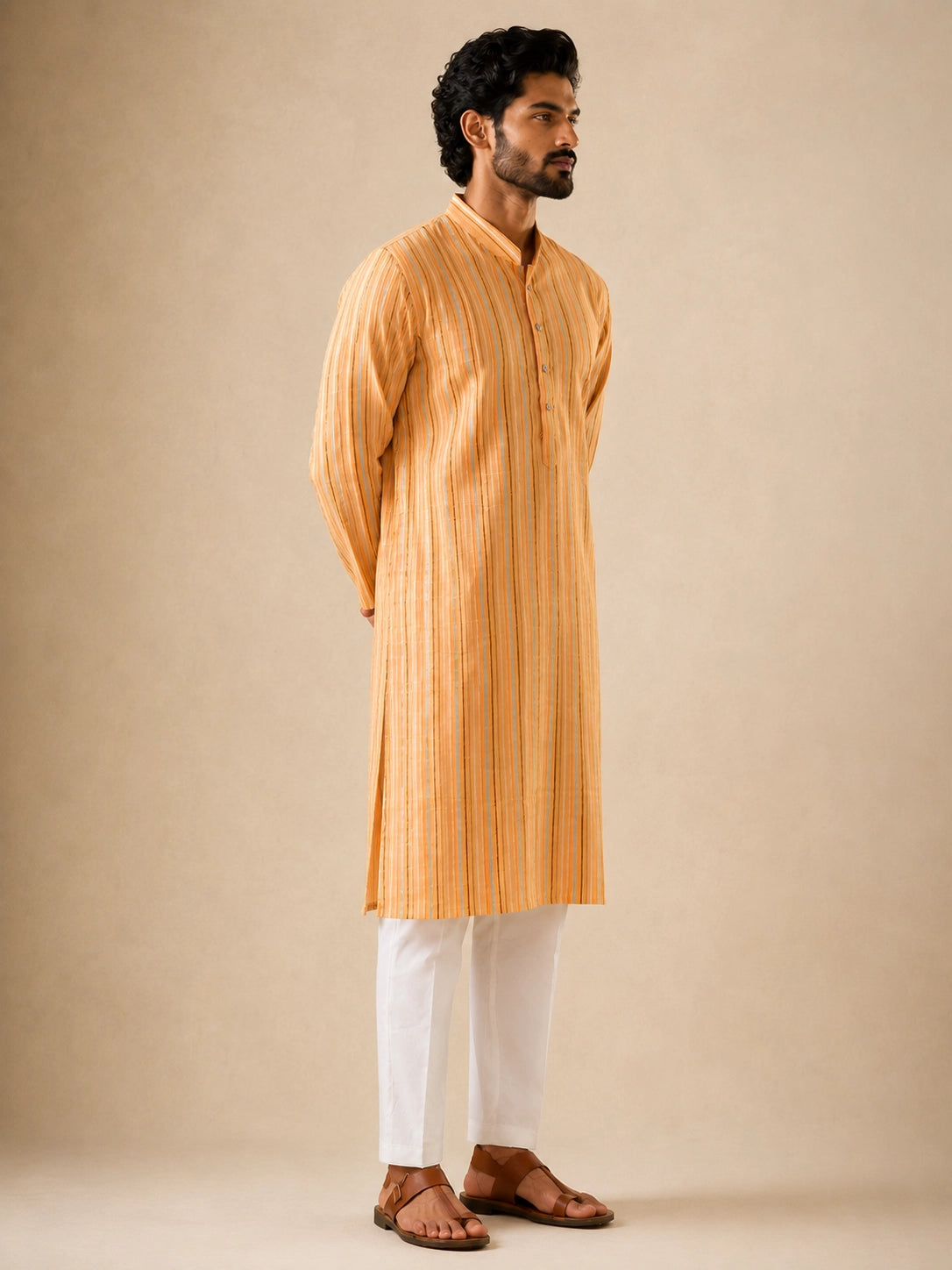 Man in a yellow striped kurta and white pajama, standing with hands behind back.