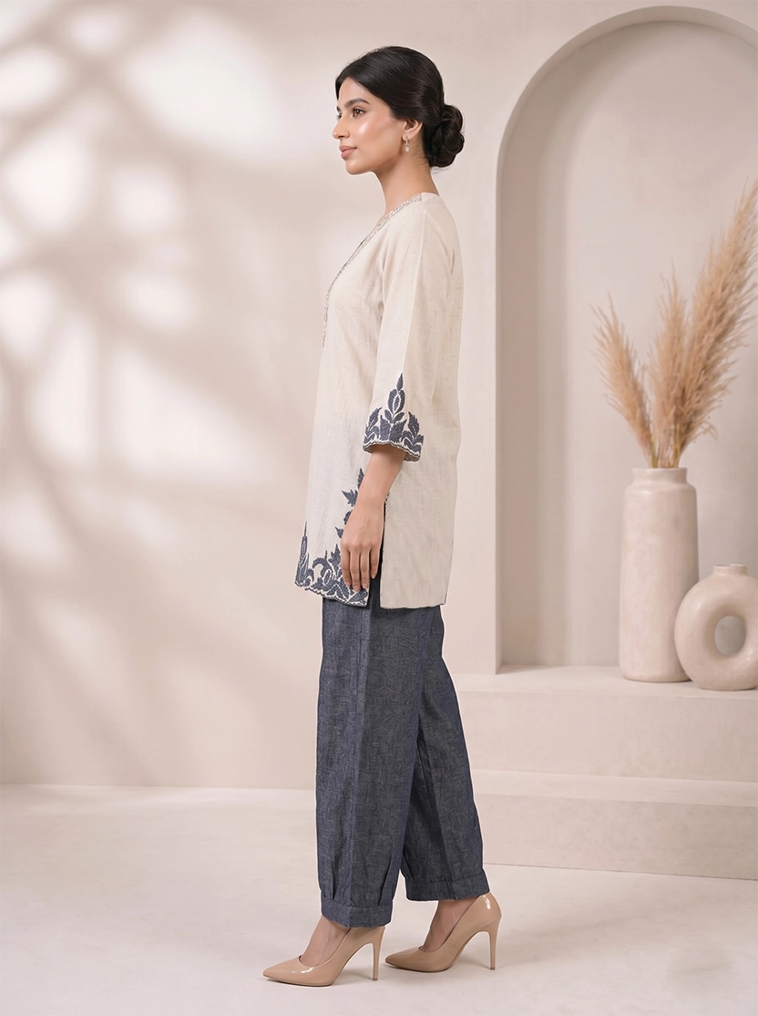 Woman wearing a beige embroidered V-neck kurta with dark blue palazzo pants, styled for a casual occasion.