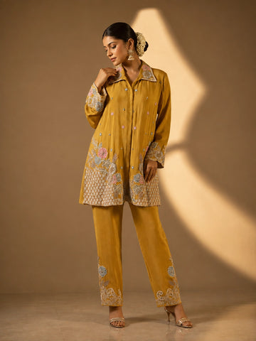 Model in a mustard embroidered kurti set with pastel floral patterns and matching pants.
