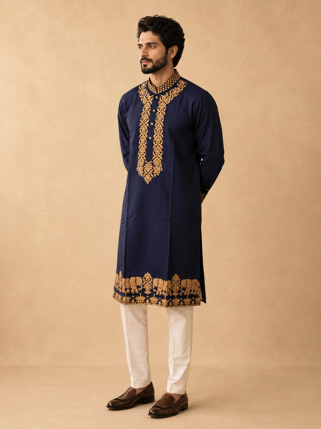 Man wearing a navy blue kurta pajama with intricate gold embroidery and elephant motifs.