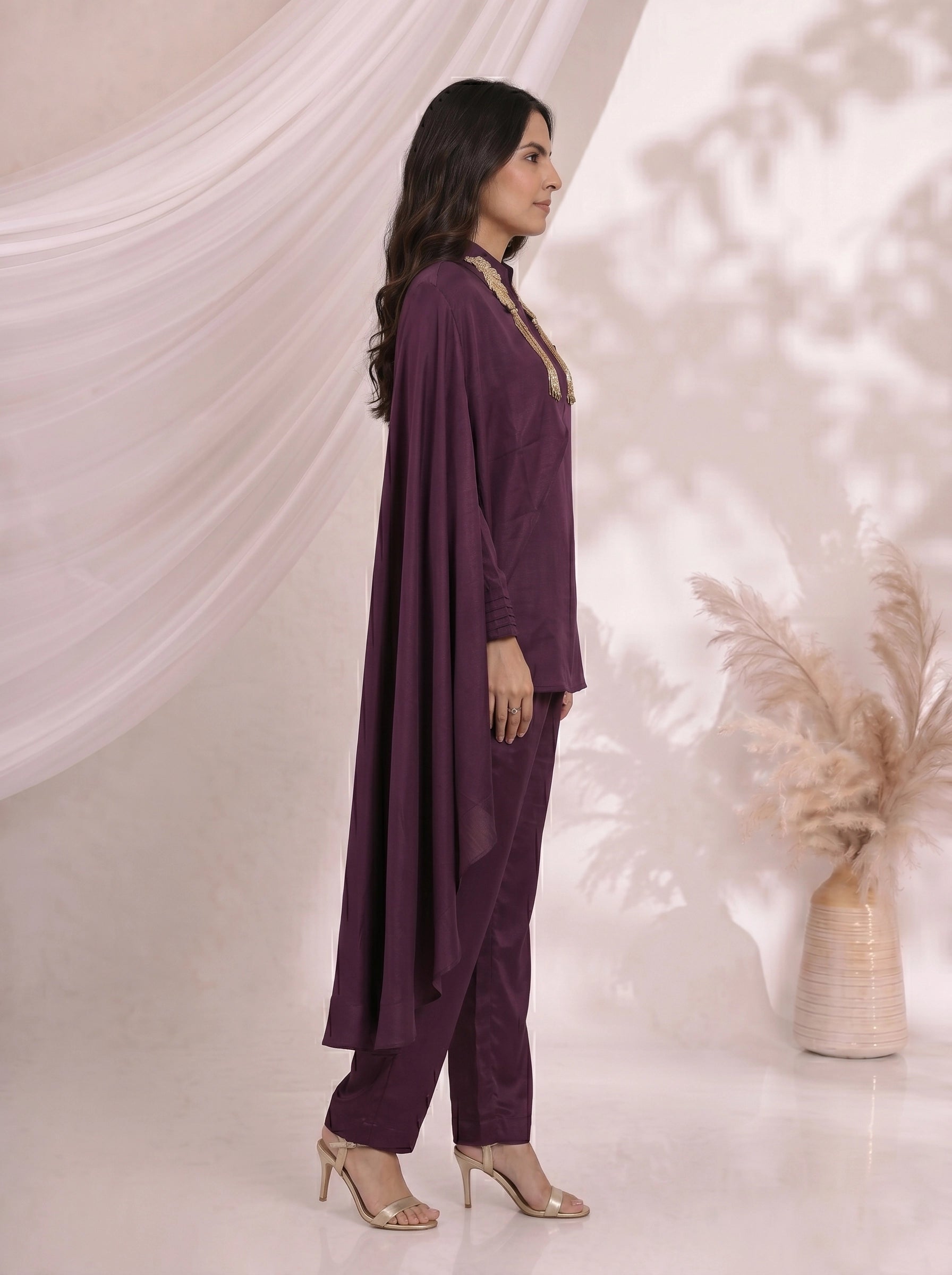 Woman wearing an elegant plum satin cape top and matching pants, styled for an evening event.
