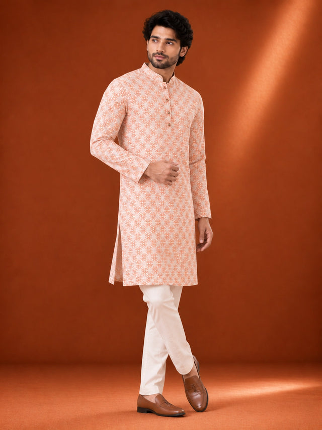 Man wearing an orange and white geometric printed kurta with white pajama and brown loafers.