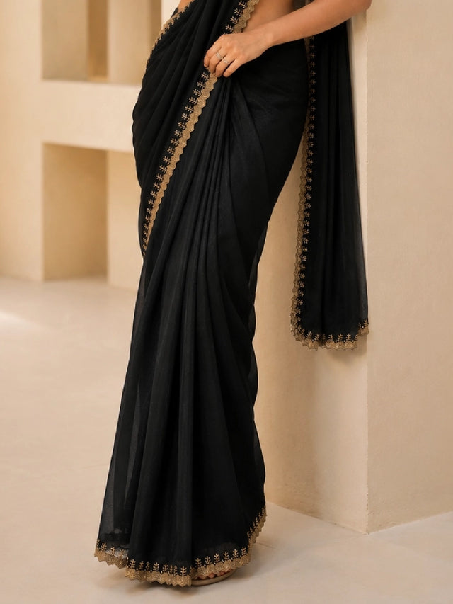 Woman in elegant black  saree with gold blouse and embroidered border.