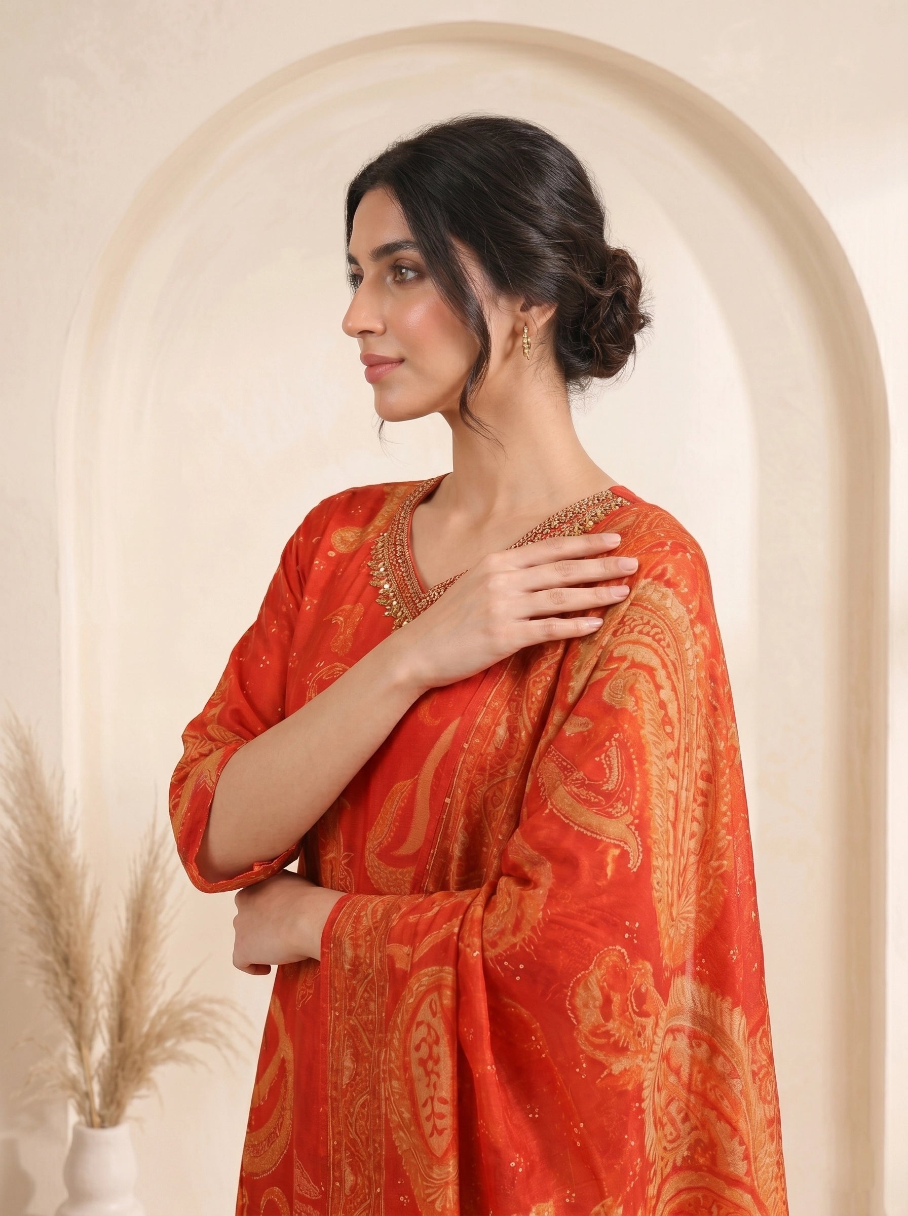 Woman wearing a vibrant orange kurti with paisley print and matching pants, adorned with neckline embellishments.