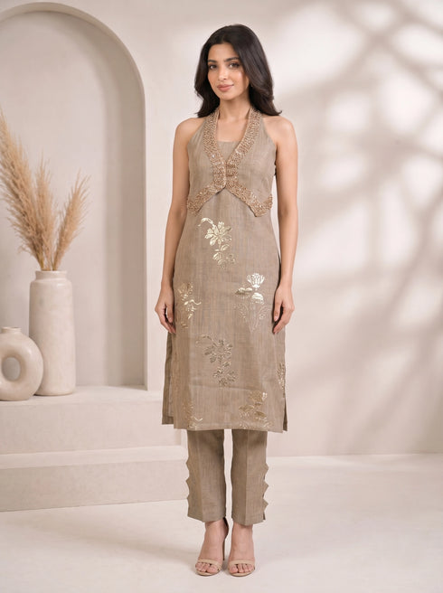 Woman wearing a khaki halter neck Kurti Set with gold floral prints and beaded neckline, paired with cut-out pants.