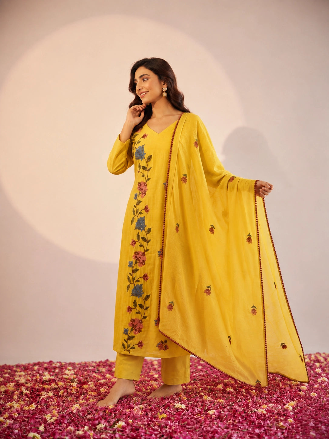 Woman in a vibrant yellow kurti set with colorful floral embroidery and dupatta.
