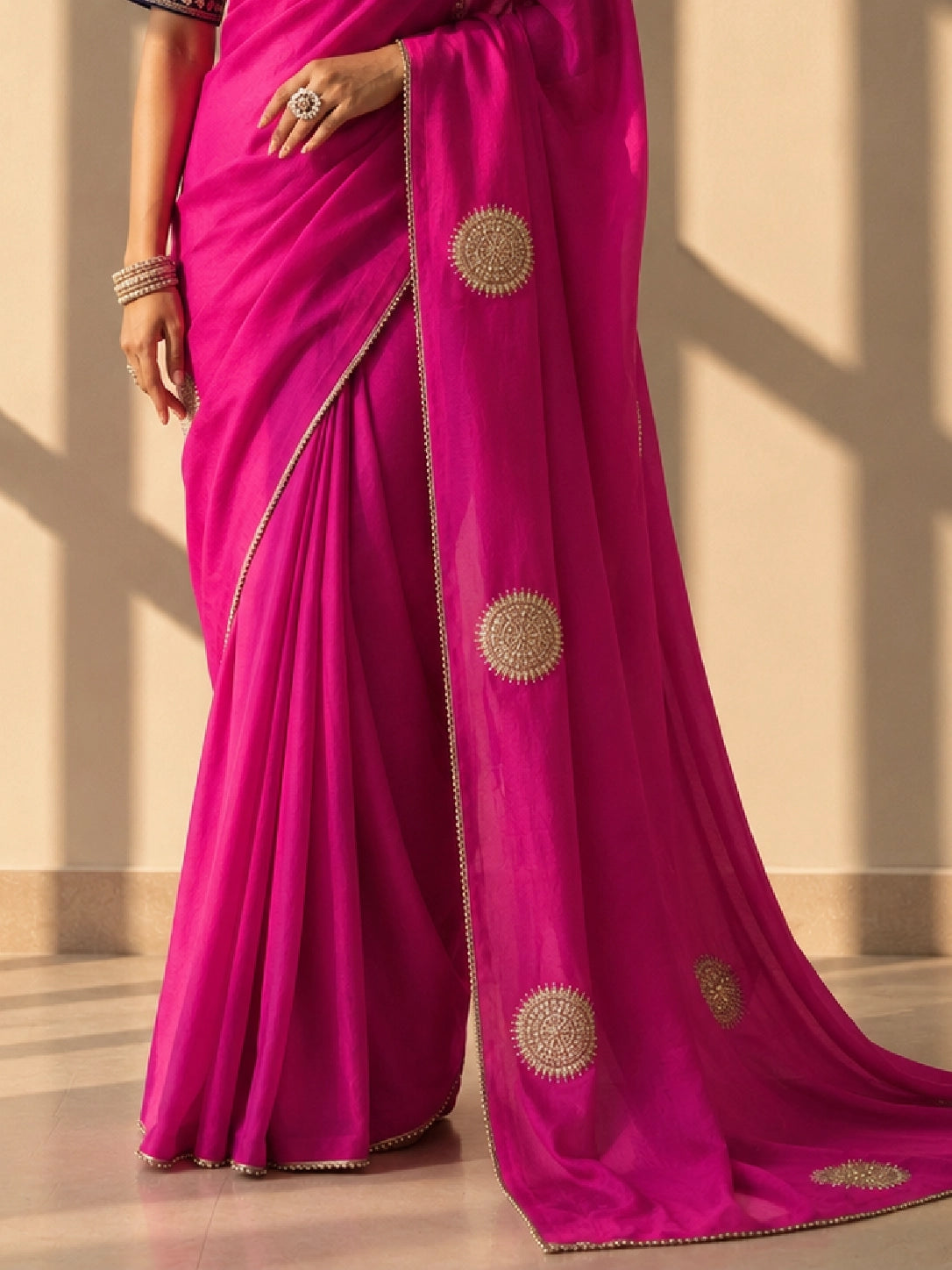 Close-up of a woman wearing a vibrant rani pink saree with gold embellished circular motifs.
