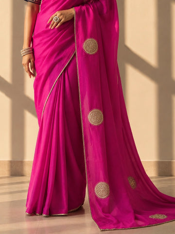 Close-up of a woman wearing a vibrant rani pink saree with gold embellished circular motifs.