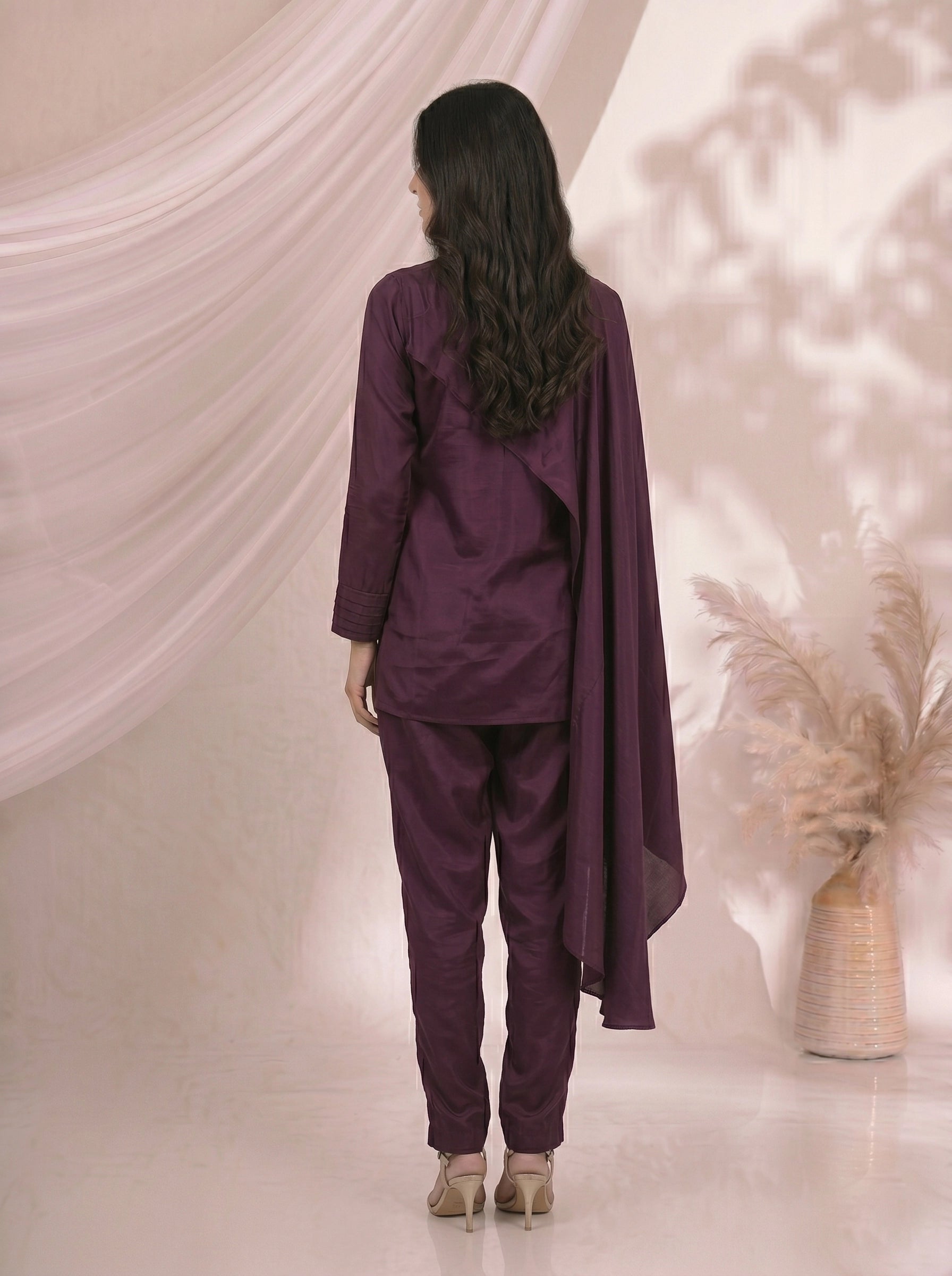 Woman wearing an elegant plum satin cape top and matching pants, styled for an evening event.