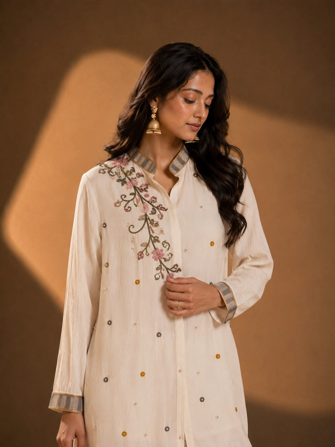 Woman wearing an elegant cream embroidered button-down kurti with striped collar and cuffs.
