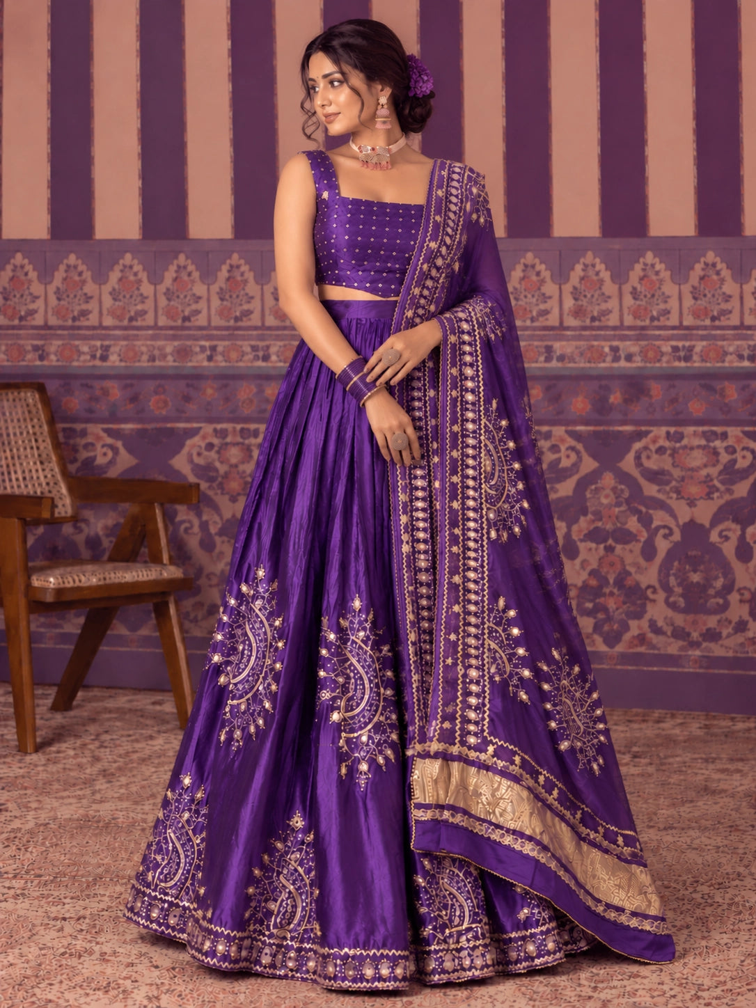 Woman in a vibrant purple embroidered lehenga choli set with gold patterns.