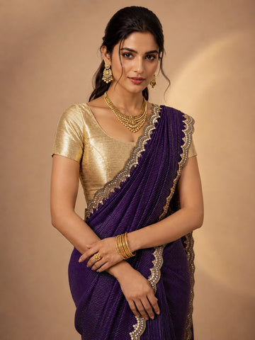 Woman wearing a vibrant purple pleated saree with an embellished border and a golden blouse.