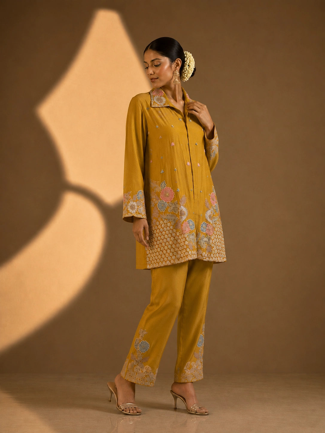 Model in a mustard embroidered kurti set with pastel floral patterns and matching pants.