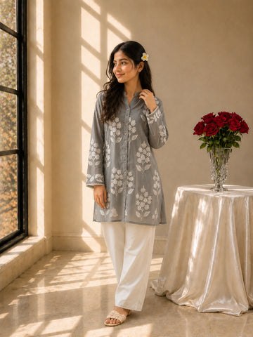 Woman wearing a sky blue embroidered tunic with white pants and sandals.