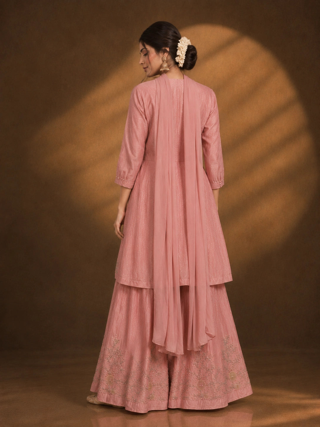 Woman in an elegant pink angrakha kurti and sharara set with intricate gold embroidery.