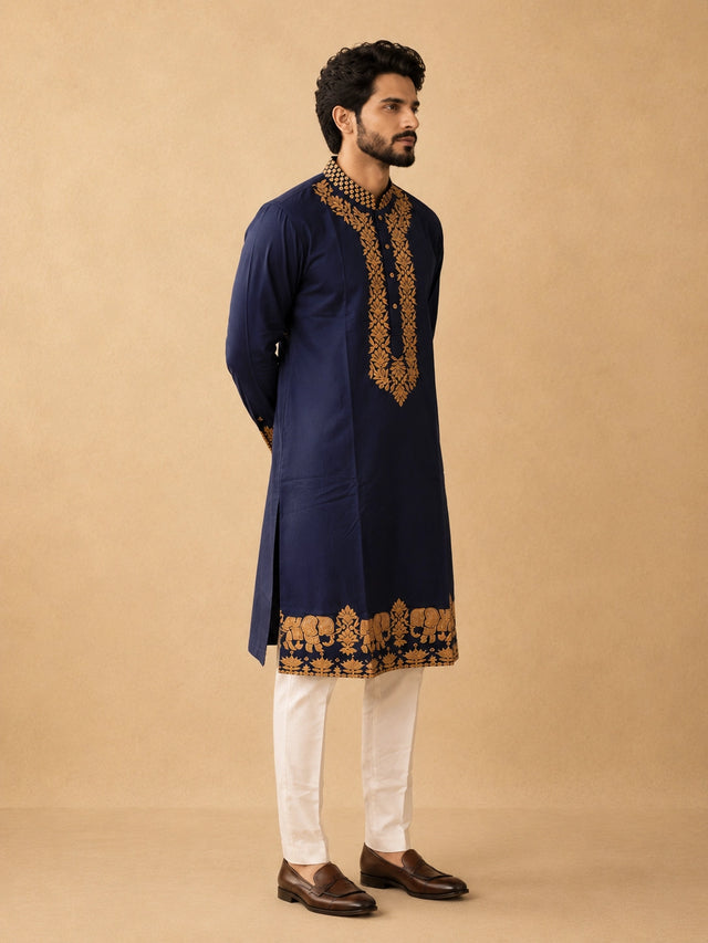 Man wearing a navy blue kurta pajama with intricate gold embroidery and elephant motifs.