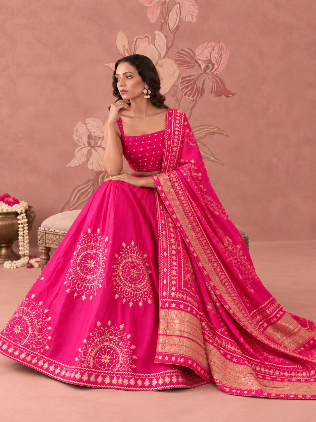 Woman wearing a vibrant rani pink lehenga set with intricate gold embroidery and matching dupatta.
